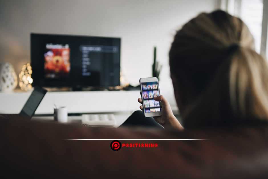 Rear view of teenage girl using smart phone app while watching TV in living room at home