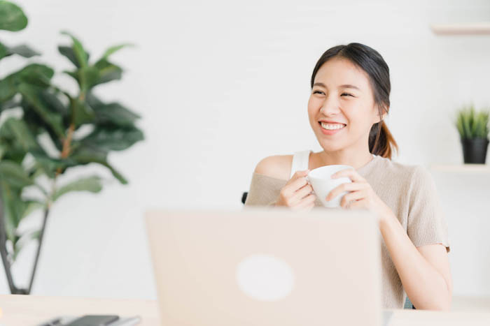 Beautiful,Young,Smiling,Asian,Woman,Working,On,Laptop,And,Drinking